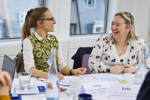 Two colleagues laughing and working together at a desk, showcasing positive team bonding and collaboration inspired by a strengths-based approach to improve workplace wellbeing.