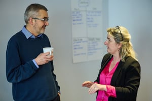 Colleagues chatting and smiling over coffee, fostering connection and workplace wellbeing.